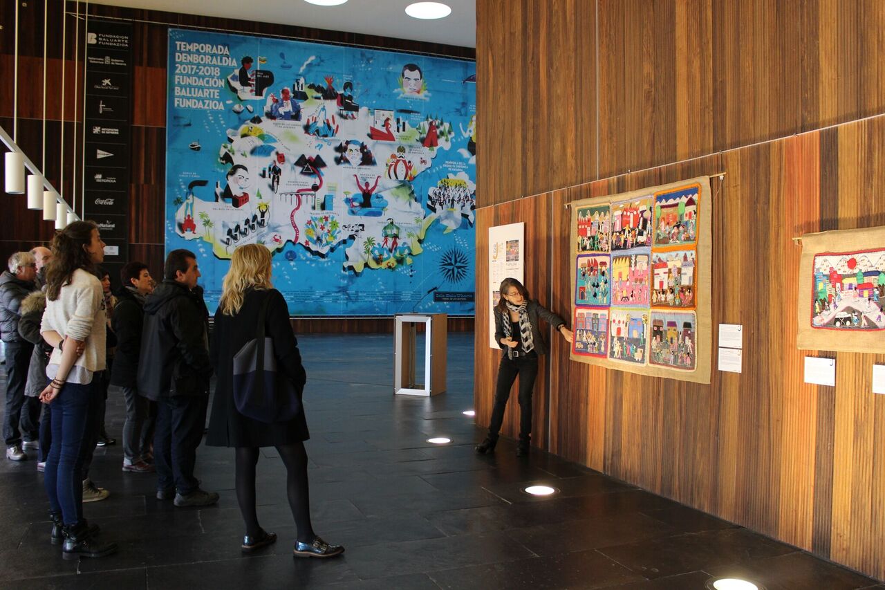 Curator Roberta Bacic gives an overview of the arpillera 'Penurias en nuestra población / Hardship in our community' as part of a guided tour of the exhibition. (Photo: Roser Corbera)